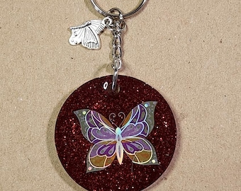 May include: A red glitter circle keychain with a silver butterfly charm. The circle features a purple and gold butterfly with iridescent wings.