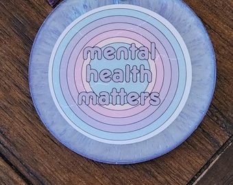 May include: A purple tassel keychain with a round, blue and pink, iridescent charm that says "mental health matters".