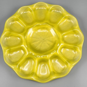 May include: A bright yellow ceramic oyster serving platter with 12 individual compartments and a central well. The platter has a scalloped edge and a glossy finish, perfect for serving appetizers or seafood. The overall shape is reminiscent of a flower.