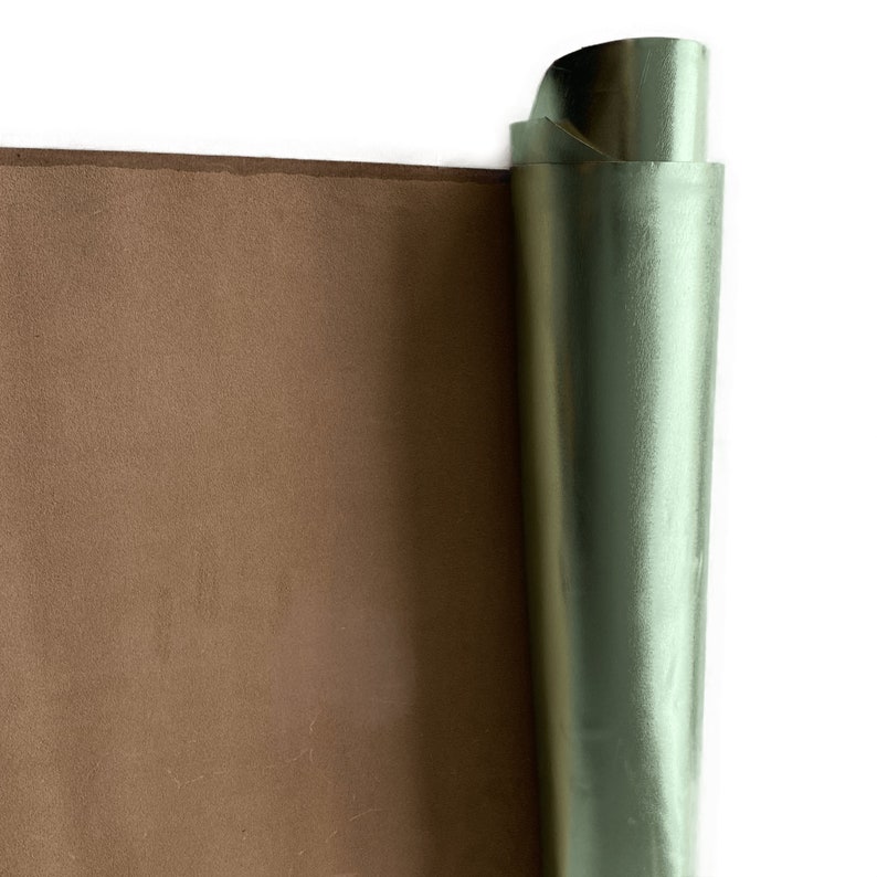 May include: A roll of brown leather next to a roll of metallic green leather. The brown leather has a matte finish, while the green leather has a shiny, reflective surface. The edges of the leather are visible.