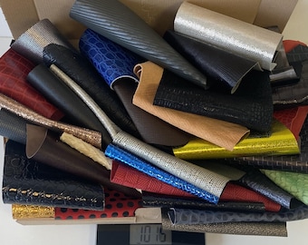 May include: A selection of leather offcuts in various colours and textures, including black, brown, red, blue and green. The offcuts are stacked on top of each other and are being weighed on a digital scale that reads 10.15.