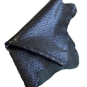 May include: A dark blue leather hide with a crocodile embossed pattern. The leather is folded in half and the edges are visible.
