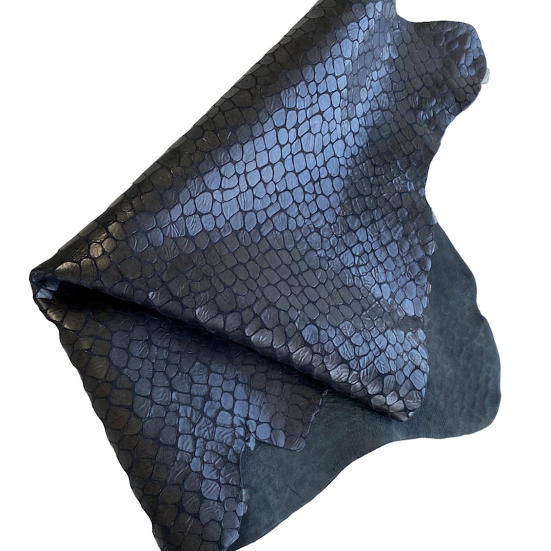 May include: A dark blue leather hide with a crocodile embossed pattern. The leather is folded in half and the edges are visible.