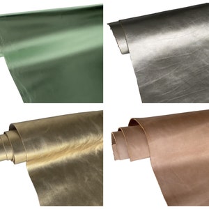 May include: Four rolls of leather in various metallic colors. The colors include green, silver, gold, and brown. The leather is rolled up, showing the texture and sheen of the material. The background is white.