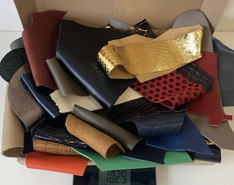 May include: A box filled with a variety of leather offcuts in different colours and textures, including black, brown, red, and gold. The offcuts are arranged in a random pattern and are being weighed on a digital scale that reads 10.29.