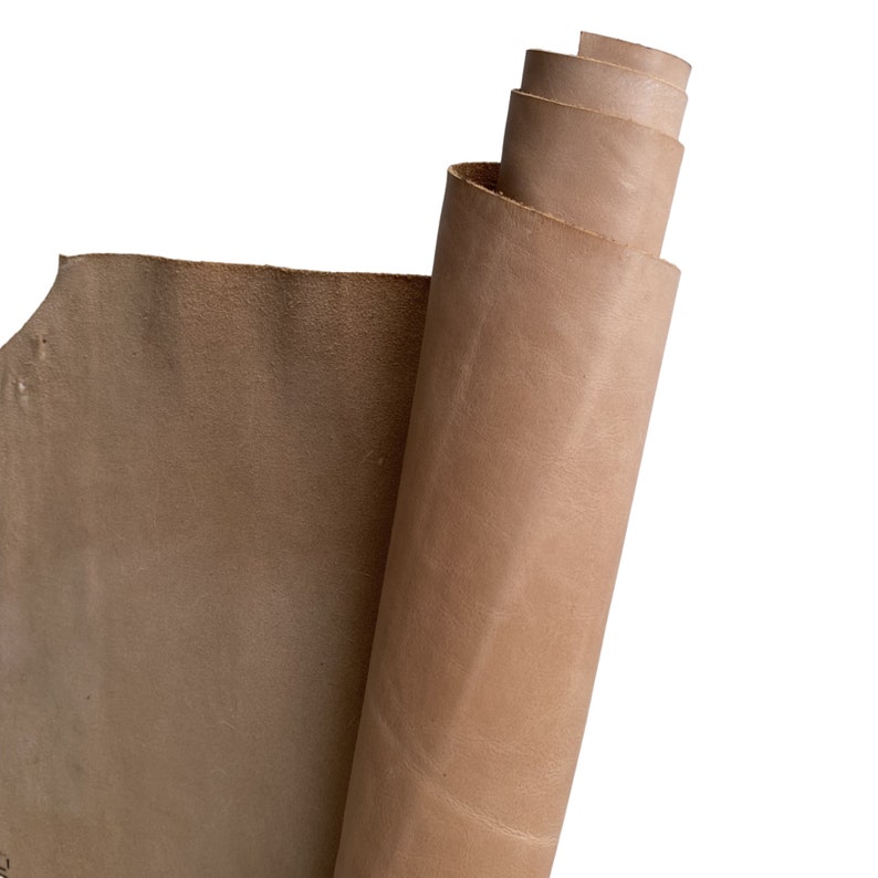 May include: A roll of natural-toned leather, partially unrolled, revealing the textured surface. The leather has a warm, neutral color, with visible grain and subtle variations in tone. The edges are slightly uneven, suggesting a raw, unfinished quality.