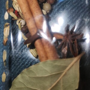 Può includere: Primo piano di una collezione di spezie ed erbe, tra cui bastoncini di cannella, anice stellato, foglie di alloro e grani di pepe. Le spezie sono disposte su uno sfondo di jeans blu.