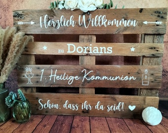 May include: A wooden pallet sign with white text that reads "Herzlich Willkommen zu Dorians 1. Heilige Kommunion Schon, dass ihr da seid!" with a white star and arrow on each side. The sign is decorated with white flowers and a white heart.