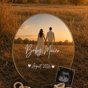 Könnte beinhalten: Ein rundes Acrylschild mit goldenem Rand, das ein Paar auf einem Feld spiegelt, mit dem weißen Text Baby Maier und dem Datum August 2026. Daneben liegen eine Holzperlenrassel, ein Paar beigefarbene Babyschuhe und ein Ultraschallbild.