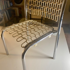 Può includere: Una sedia in metallo cromato e bianco con una seduta e uno schienale intrecciati unici. La sedia ha un design semplice e moderno.