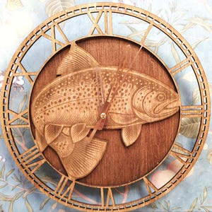 May include: Wooden clock featuring a detailed fish design. The clock has a dark brown circular face with a fish carving in the center. The outer ring is a lighter brown with Roman numerals. The clock hands are a light brown color.