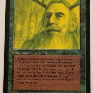 May include: A green Magic: The Gathering card with the name "Gaea's Liege" and a green illustration of a man with antlers. The card text reads: "Summon Gaea's Liege. When defending, Gaea's Liege has power and toughness equal to the number of forests you have in play; when it's attacking, they are equal to the number of forests opponent has in play. Tap to turn any one land into a forest until Gaea's Liege leaves play. Mark changed lands with counters, removing the counters when Gaea's Liege leaves play."