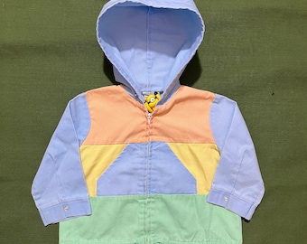 May include: A colorful hooded jacket with a full zipper closure. The jacket features a light blue hood and sleeves, with a color block design of peach, yellow, and green panels on the front. The zipper pull has a cartoon character.