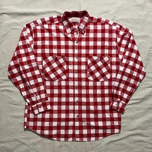 May include: A red and white checkered button-down shirt with two front pockets. The long-sleeved shirt has a classic gingham pattern and a button-down collar. The shirt is made of a soft, woven fabric.