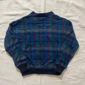 May include: A blue, green, and red plaid bomber jacket. The jacket has a navy blue collar, cuffs, and waistband. The plaid pattern is a classic design, with a mix of blue, green, and red lines.