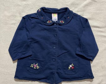 May include: A navy blue jacket with a rounded collar and two front pockets, embroidered with colourful floral designs. The jacket has three-quarter length sleeves and a tag that reads "6-12 mos.".