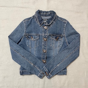 May include: A blue denim jacket with a button closure and two front pockets. The jacket has a small white heart embroidered on the left pocket.