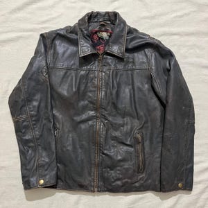 May include: A dark brown leather jacket with a zipper closure and a "Pirates of the Caribbean" logo on the left chest.