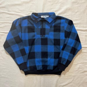 May include: Blue and black plaid fleece pullover with a quarter-zip closure. The long-sleeved top has a collared neckline and ribbed cuffs and hem. The tag reads "Timber Bay".