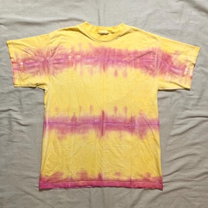 May include: Yellow t-shirt with a tie-dye pattern in shades of pink. The short-sleeved shirt has a crew neck and a horizontal stripe design across the chest and lower torso. The fabric appears to be cotton.