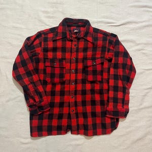 Pode incluir: Uma camisa de flanela xadrez vermelha e preta com fecho de botões e dois bolsos no peito.