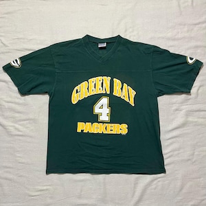 Puede incluir: Una camiseta verde con cuello en V con las palabras "GREEN BAY" arqueadas en el pecho en amarillo, con el número "4" en blanco y la palabra "PACKERS" debajo. Las mangas tienen un logotipo verde y amarillo. La camiseta es de material suave.