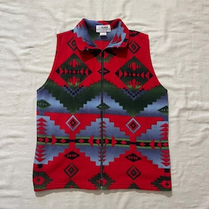 May include: A sleeveless fleece vest with a vibrant geometric pattern in red, blue, and green. The vest has a full-length zipper and a collared neckline. The pattern includes diamond and arrow shapes. The vest is a medium size.