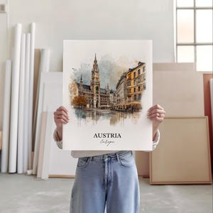 May include: A watercolour print depicting a European city, with a prominent building featuring a spire and other structures in shades of brown, yellow, and grey. The print is labelled "AUSTRIA Europe". The print is held by a person.