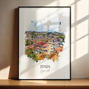 Op de afbeelding: Een ingelijste aquarelprint van Jinja, Oeganda. Het kunstwerk toont een kleurrijk stadsbeeld met gebouwen, bomen en een blauwe lucht. De print heeft een zwarte lijst en de tekst "Jinja Uganda" is in een scriptletter geschreven.