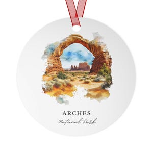 May include: A round, white ornament with a watercolor image of Delicate Arch in Arches National Park, Utah. The text "ARCHES National Park" is printed below the image.