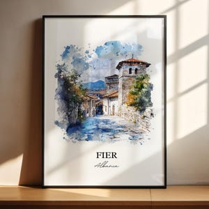 May include: A framed watercolor print of a European town scene. The artwork features a stone street leading to buildings with red-tiled roofs and a tall tower. The word "FIER" and "Albania" are printed at the bottom of the print.