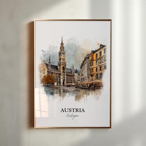 May include: A framed watercolour print depicting a European city, with a gold-coloured frame. The image shows a detailed view of a historic building with a tall tower, other buildings, and a street scene. The text "AUSTRIA Europe" is at the bottom.