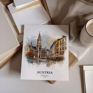 May include: A square print with a watercolour illustration of a European city, including a tall clock tower. The print has the words "AUSTRIA Europe" at the bottom. The print is on a white surface.