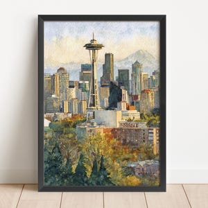 May include: Watercolor painting of the Seattle skyline, featuring the Space Needle and surrounding buildings. The artwork is framed in black and depicts a sunny day with a mountain in the background. The foreground shows trees.
