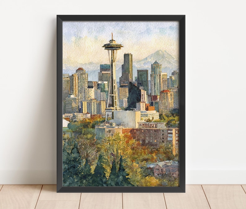 May include: Watercolor painting of the Seattle skyline, featuring the Space Needle and surrounding buildings. The artwork is framed in black and depicts a sunny day with a mountain in the background. The foreground shows trees.