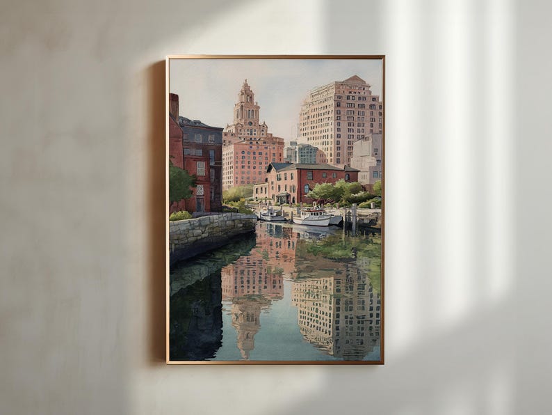 May include: Watercolor painting of a city waterfront scene. Buildings in shades of red and beige line the water's edge, with reflections in the water. Several white boats are docked. The artwork is framed in a gold-colored frame.