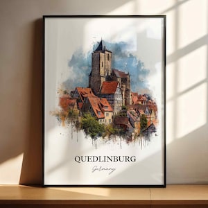 Op de afbeelding: Ingelijste kunstdruk met een aquarel schilderij van Quedlinburg, Duitsland. Het kunstwerk toont een historische stad met rode pannendaken, een hoge kerktoren en de tekst "Quedlinburg Germany". De print zit in een zwart frame.