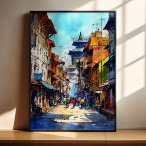 Puede incluir: Una pintura de acuarela enmarcada representa una escena callejera vibrante. Edificios con fachadas coloridas bordean la carretera, con gente caminando por el camino soleado. El cielo es azul brillante y la obra está enmarcada en negro.