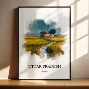 May include: Framed watercolor print of a rural landscape in Uttar Pradesh, India. The artwork depicts a field of golden grass, a small stream, and a cluster of buildings under a cloudy sky. The text "UTTAR PRADESH India" is printed at the bottom.