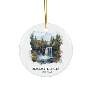 Könnte beinhalten: Runder, weißer Keramikschmuck mit einem Aquarellgemälde des Blackwater Falls State Park. Das Bild zeigt einen Wasserfall über einer felsigen Klippe, umgeben von Bäumen mit Herbstlaub. Der Text "BLACKWATER FALLS State Park" ist darunter gedruckt.