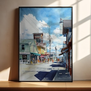 May include: Watercolor painting of a street scene with buildings and people. The artwork features a blue sky with clouds, a street with shadows, and colorful buildings. The painting is framed in a black border.