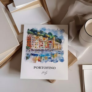Op de afbeelding: Een aquarel schilderij van kleurrijke gebouwen in Portofino, Itali&euml;. De gebouwen zijn geclusterd op een heuvel met uitzicht op een haven met boten. Het schilderij heeft een zachte, dromerige uitstraling.