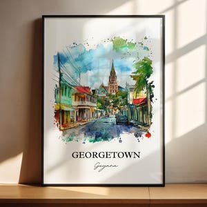 May include: A framed watercolor print of Georgetown, Guyana. The artwork depicts a street scene with colorful buildings, a church steeple, and a car on the road. The text "GEORGETOWN Guyana" is printed at the bottom.