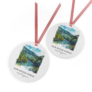 Könnte beinhalten: Zwei runde, weiße Ornamente mit einem Aquarellbild einer Brücke über einem Fluss. Der Text "NEW RIVER GORGE West Virginia" ist auf jedem Ornament aufgedruckt.
