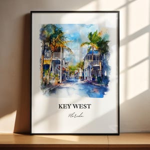 May include: A watercolor painting of a street scene in Key West, Florida. The painting features colorful buildings with palm trees lining the street. The text "KEY WEST" and "Florida" is printed below the image.
