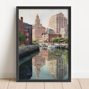 May include: Watercolor painting of a city waterfront scene with buildings and boats. The artwork features a reflection of the buildings in the water. The buildings are in shades of red, brown, and beige. The artwork is framed in a black frame.