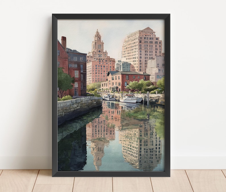 May include: Watercolor painting of a city waterfront scene with buildings and boats. The artwork features a reflection of the buildings in the water. The buildings are in shades of red, brown, and beige. The artwork is framed in a black frame.