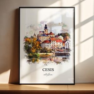 May include: Framed watercolor print of Cesis, Latvia, featuring a detailed depiction of the town's architecture, including a church with a tall steeple and buildings with red tile roofs. The print has a black frame and the text "Cesis Latvia" at the bottom.