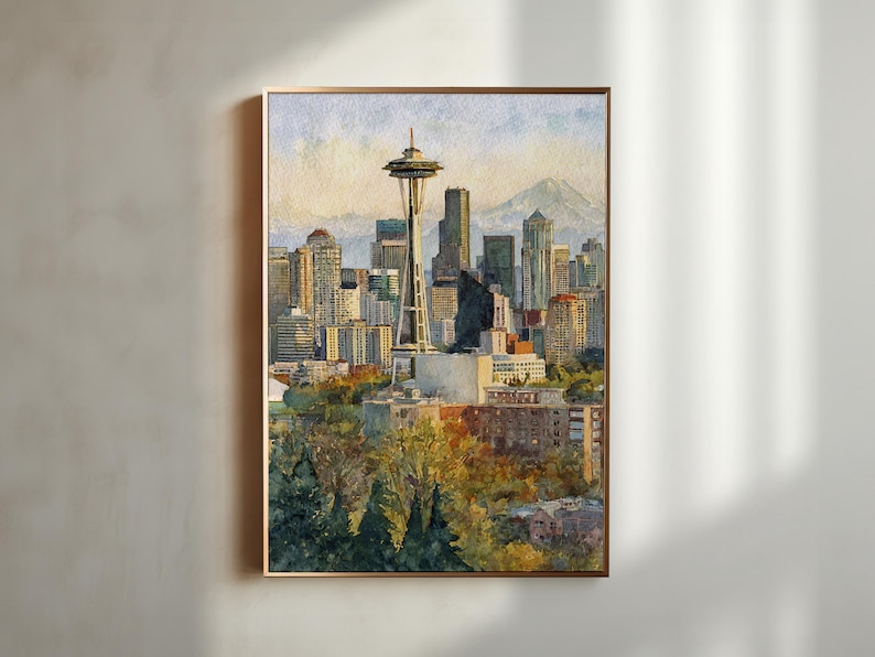 May include: Watercolor painting of the Seattle skyline, featuring the Space Needle and surrounding skyscrapers. The artwork is framed in a gold-colored border and depicts a sunny day with a mountain in the background.