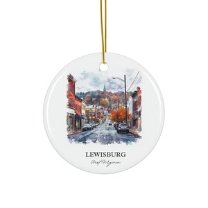 Könnte beinhalten: Weißer Keramik-Weihnachtsschmuck mit einem Aquarellgemälde von Lewisburg, West Virginia. Das Bild zeigt eine Straßenszene mit Gebäuden, Autos und einem Kirchturm. Ein goldener Faden ist zum Aufhängen befestigt.